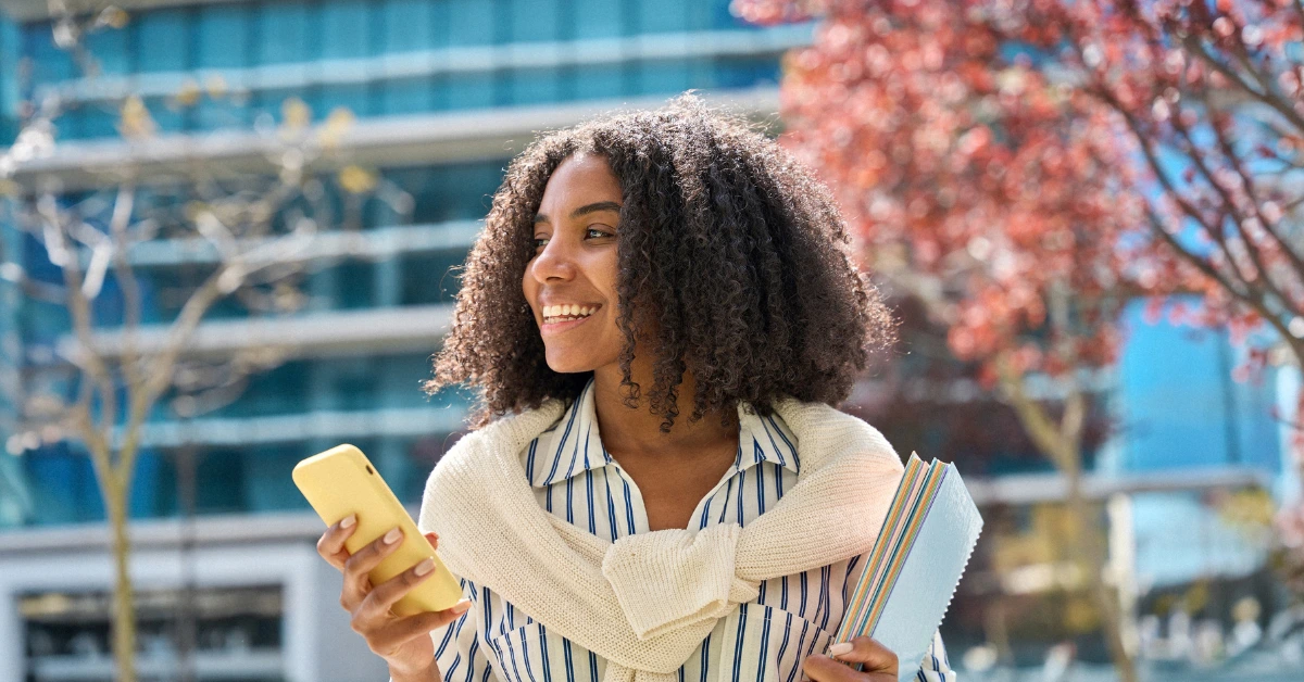Mulher estudante alegre segurando materiais de estudo e celular.