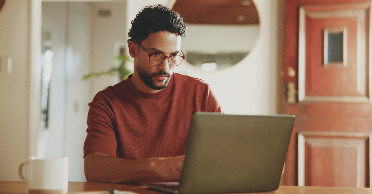 Homem de óculos estudando Atualidades no seu notebook sobre a mesa.
