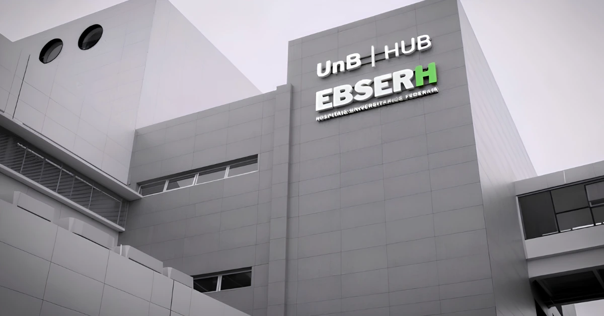 Fachada de um edifício moderno na cor cinza com o letreiro da EBSERH em destaque, com a letra H em verde. Acima, lê-se 'UnB | HUB' e, abaixo, 'Hospitais Universitários Federais'.